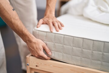 Young hispanic man holding mattress at bedroom