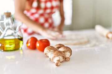 Young beautiful hispanic woman kneading dough pizza with hands at the kitchen