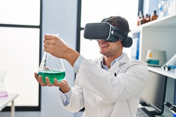 Young hispanic man scientist using virtual reality glasses holding test tube at laboratory