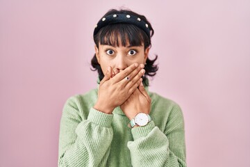 Young beautiful woman standing over pink background shocked covering mouth with hands for mistake....