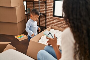 Mother and son using smartphone sitting on sofa at new home