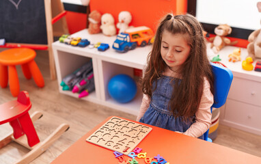 Fototapeta premium Adorable hispanic girl playing with maths puzzle game sitting on table at kindergarten