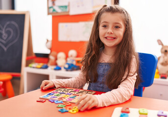 Adorable hispanic girl playing with maths puzzle game sitting on table at kindergarten