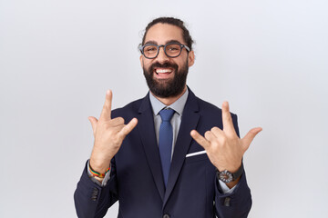 Hispanic man with beard wearing suit and tie shouting with crazy expression doing rock symbol with hands up. music star. heavy concept.