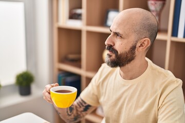 Young bald man drinking coffee sitting on table at home