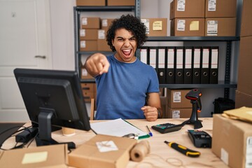 Hispanic man with curly hair working at small business ecommerce pointing displeased and frustrated to the camera, angry and furious with you