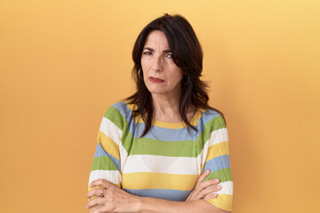 Middle age hispanic woman standing over yellow background skeptic and nervous, disapproving expression on face with crossed arms. negative person.