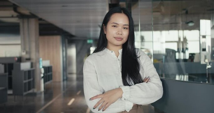 Confident Asian girl posing in a white shirt against the backdrop of the office. Way to success