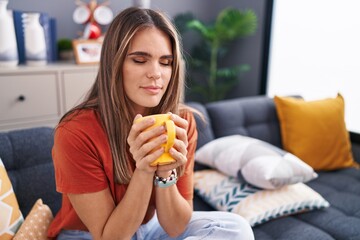 Young beautiful hispanic woman drinking coffee sitting on sofa at home