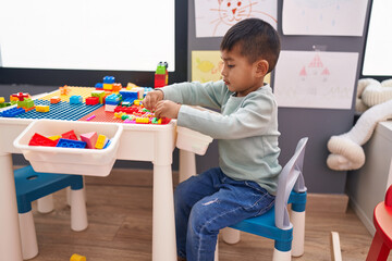 Adorable hispanic boy playing with construction blocks sitting on table at kindergarten