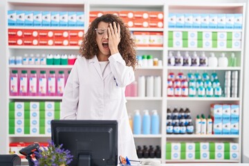 Hispanic woman with curly hair working at pharmacy drugstore yawning tired covering half face, eye and mouth with hand. face hurts in pain.