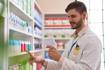 Young caucasian man pharmacist reading prescription holding product of shelving at pharmacy