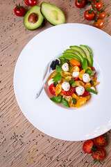 top view salad with avacado, mozzarella and tomatoes in a white plate
