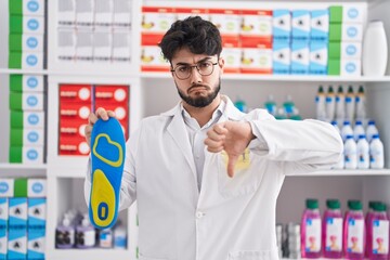 Hispanic man with beard working at pharmacy drugstore holding insole with angry face, negative sign...
