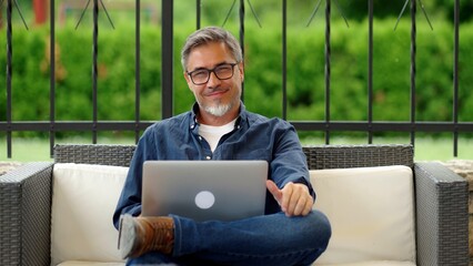 Man working with laptop computer outdoor, sitting in garden at home, managing business online from...