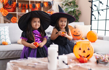 Adorable twin girls having halloween party holding pumpkin baskets at home