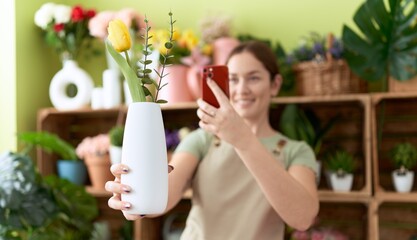 Young beautiful woman florist make photo to flower by smartphone at flower shop