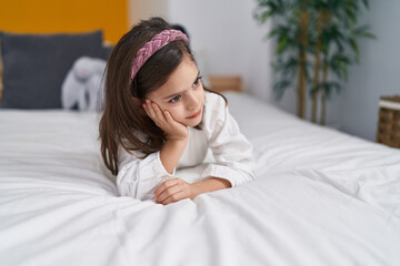 Adorable hispanic girl lying on the bed with sad expression at bedroom