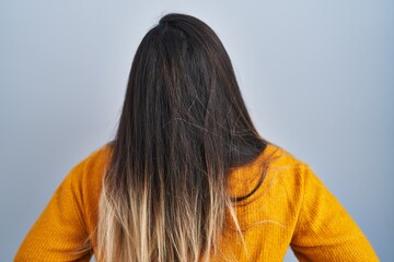 Young hispanic woman standing over isolated background standing backwards looking away with arms on body