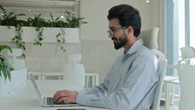 Arabian Indian muslim businessman man working on internet use laptop male professional entrepreneur office employee worker ceo manager studying online on computer remote job browsing web data smiling