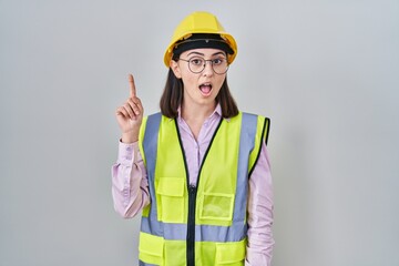 Hispanic girl wearing builder uniform and hardhat pointing finger up with successful idea. exited and happy. number one.