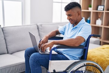 Young latin man using laptop sitting on wheelchair at home