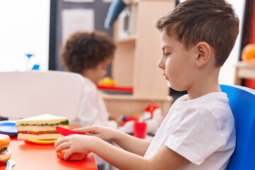 Adorable boys playing with food toy sitting on table at kindergarten