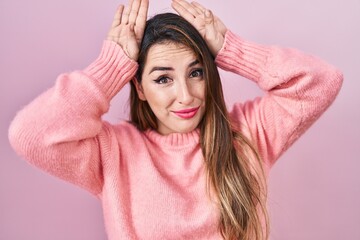 Young hispanic woman standing over pink background doing bunny ears gesture with hands palms looking cynical and skeptical. easter rabbit concept.