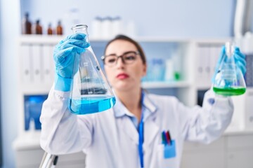 Young beautiful hispanic woman scientist holding test tubes at laboratory