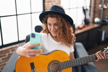 Young beautiful hispanic woman musician playing classical guitar make selfie by smartphone at music studio