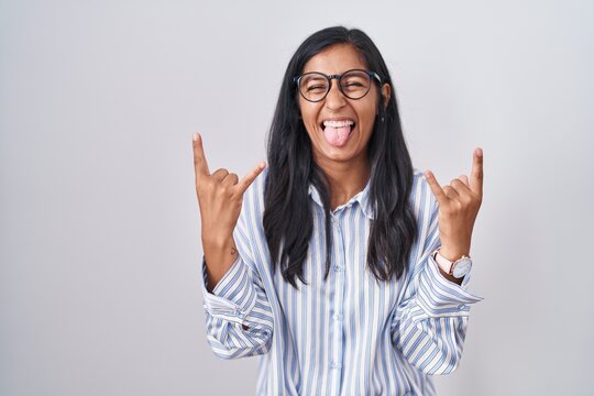 Young hispanic woman wearing glasses shouting with crazy expression doing rock symbol with hands up. music star. heavy music concept.
