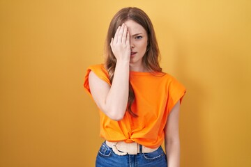 Caucasian woman standing over yellow background yawning tired covering half face, eye and mouth with hand. face hurts in pain.