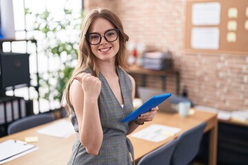 Caucasian woman working at the office wearing glasses pointing to the back behind with hand and thumbs up, smiling confident