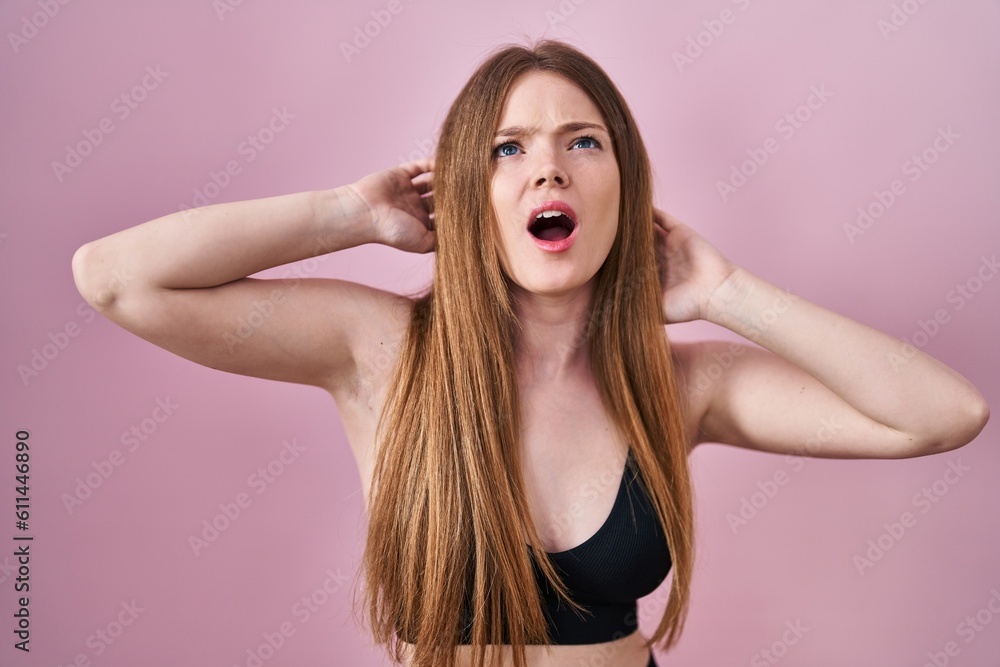 Poster young caucasian woman wearing lingerie over pink background angry and mad screaming frustrated and f