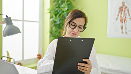 Middle eastern woman doctor reading clipboard thinking at clinic
