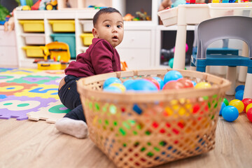Adorable hispanic boy playing with balls sitting on floor at kindergarten