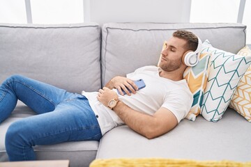 Fototapeta na wymiar Young caucasian man listening to music lying on sofa at home