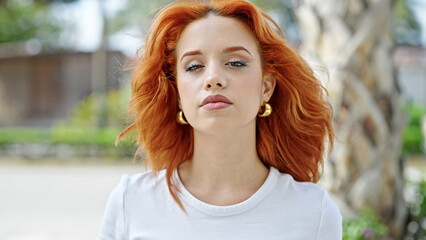 Young redhead woman standing with relaxed expression at park