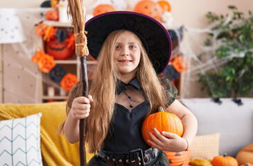 Adorable blonde girl wearing witch costume holding broom at home