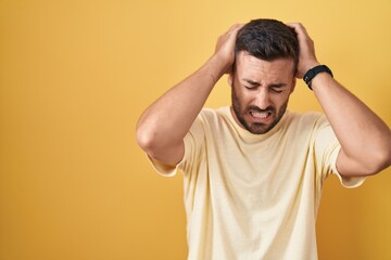 Fototapeta na wymiar Handsome hispanic man standing over yellow background suffering from headache desperate and stressed because pain and migraine. hands on head.