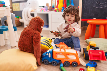 Adorable hispanic boy playing with car and dinosaur toy sitting on floor at kindergarten