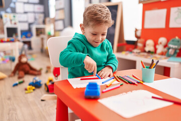 Adorable caucasian boy preschool student sitting on table drawing on notebook at kindergarten