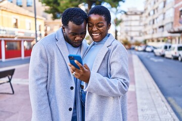 Man and woman couple standing together using smartphone at street