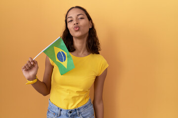 Young hispanic woman holding brazil flag looking at the camera blowing a kiss on air being lovely...