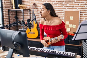 Fototapeta na wymiar Young african american woman musician singing song playing ukelele at music studio