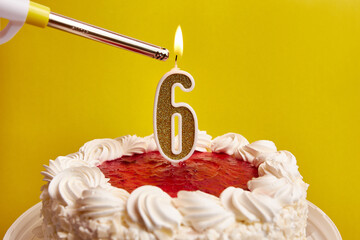 A candle in the form of the number 6, stuck in a festive cake, is lit. Celebrating a birthday or a...