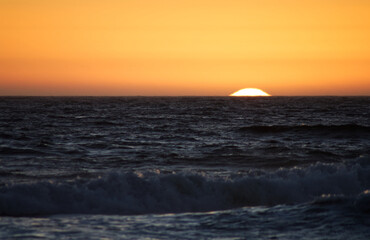 Setting Sun Over Ocean Waves With Orange Sky