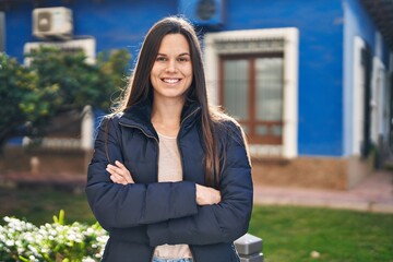 Young beautiful hispanic woman standing with arms crossed gesture at park