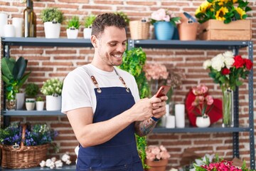 Young hispanic man florist smiling confident using smartphone at florist