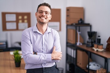 Fototapeta premium Young hispanic man at the office happy face smiling with crossed arms looking at the camera. positive person.